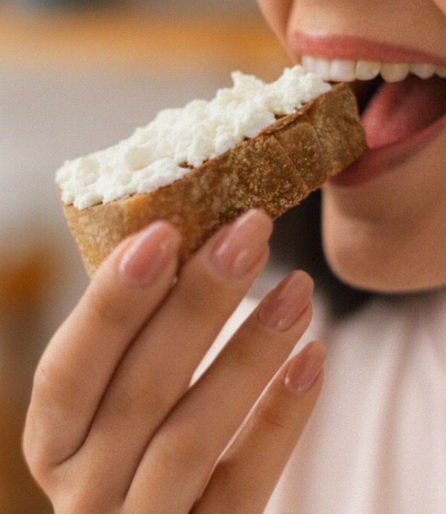 Donna che assapora una fetta di pane con feta, simbolo di una pausa gustosa e genuina con i sapori autentici greci Kionas.