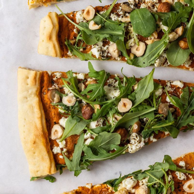 Pizza con crema di peperoni, formaggio greco, rucola e nocciole