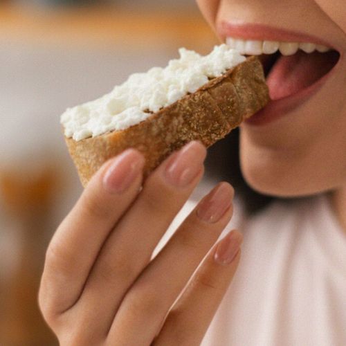 Donna che assapora una fetta di pane con feta, simbolo di una pausa gustosa e genuina con i sapori autentici greci Kionas.