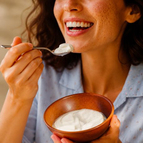 Donna sorridente mentre mangia yogurt greco da una ciotola
