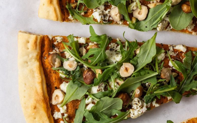 Pizza con crema di peperoni, formaggio greco, rucola e nocciole